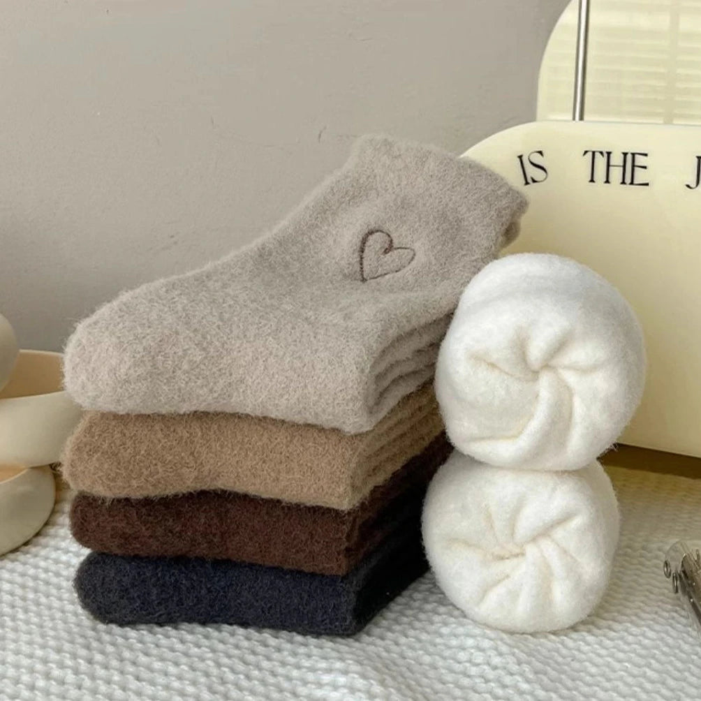 Stack of Warm Velvet Heart Socks in cream, beige, brown, and black shades, neatly folded on a white knitted surface.