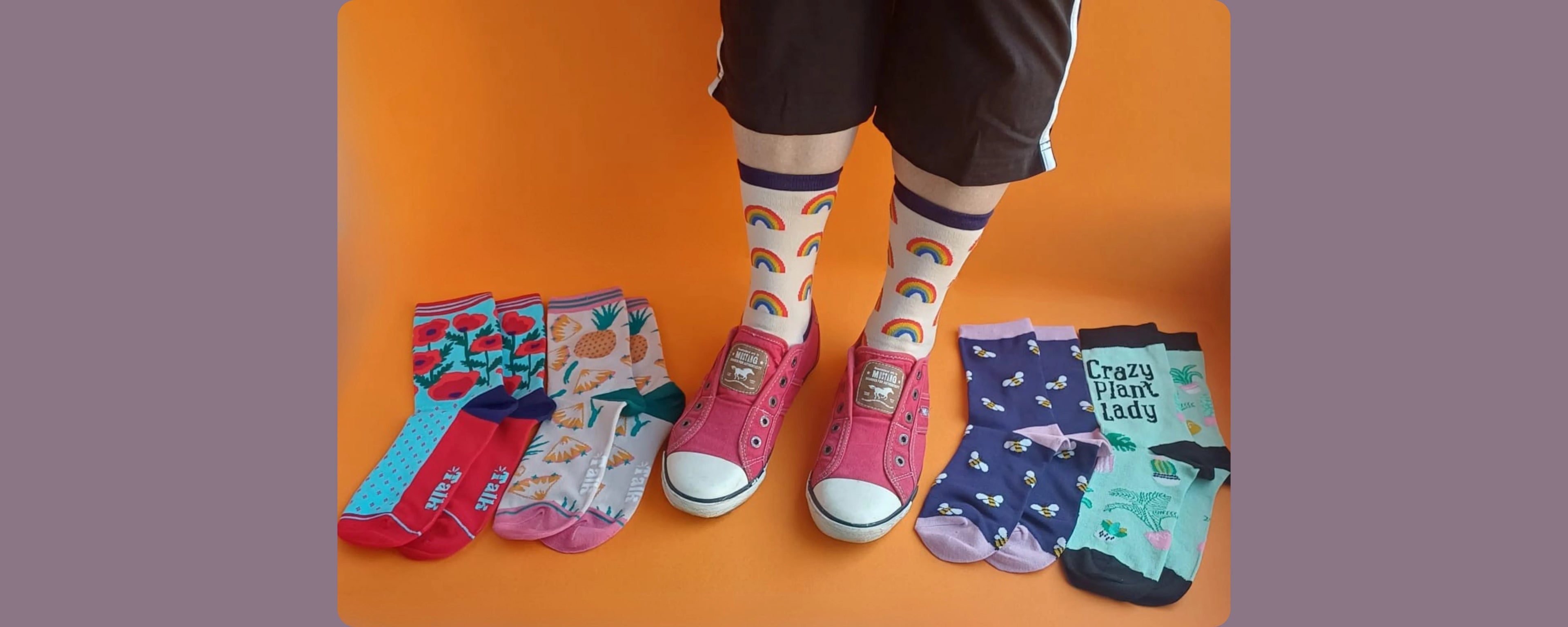 Colourful womens socks laid out on an orange background with a person wearing rainbow bamboo socks