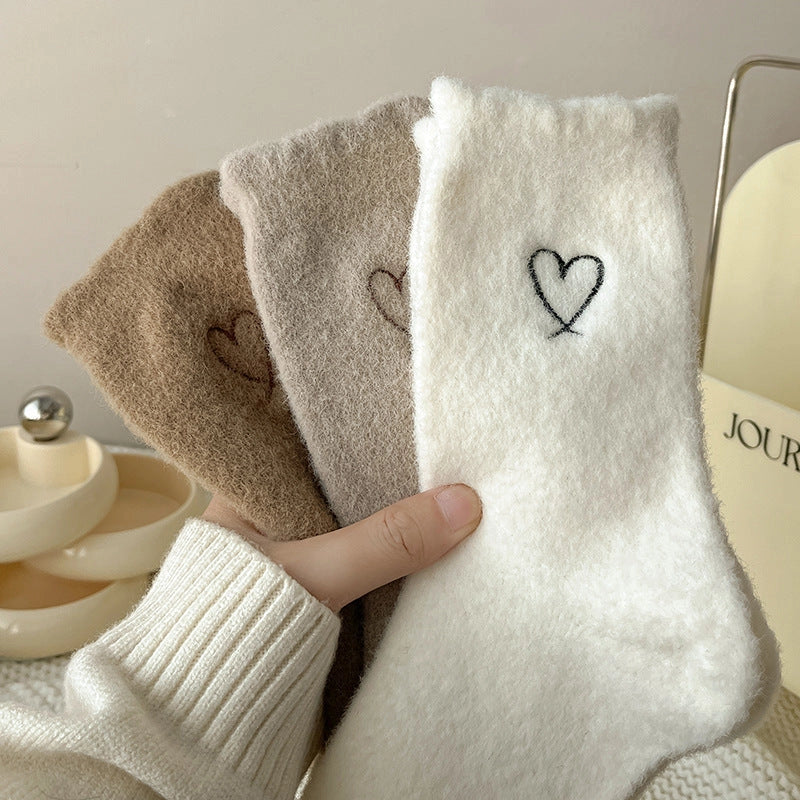 Hand holding Warm Velvet Heart Socks in cream, beige, and brown colours, showing heart embroidery on each pair.